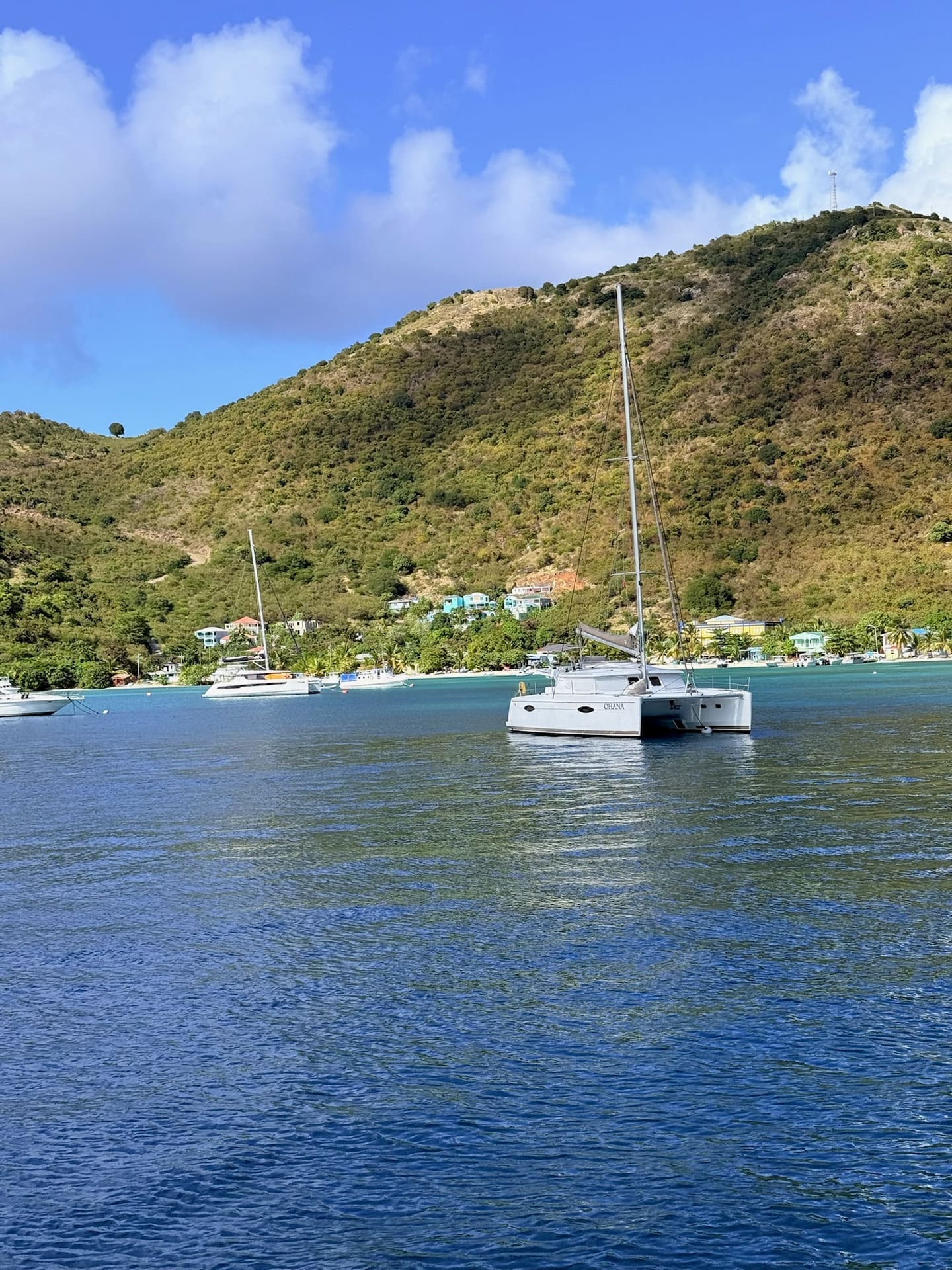 Our catamaran anchored in bright turquoise water below a green island headland under a blue sky